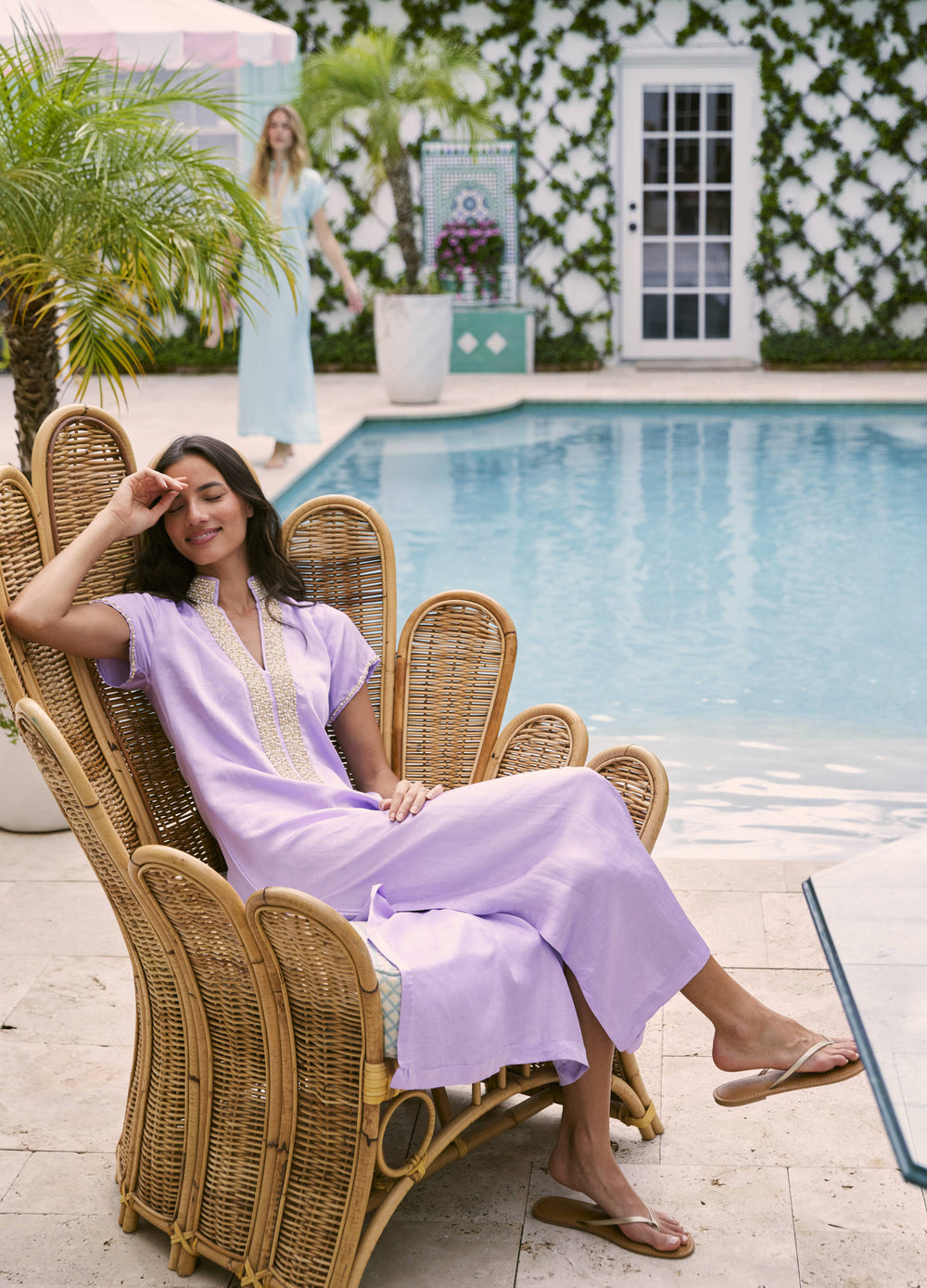 Pearl Cap Sleeve Caftan in Lilac, seated in a wicker chair by the pool