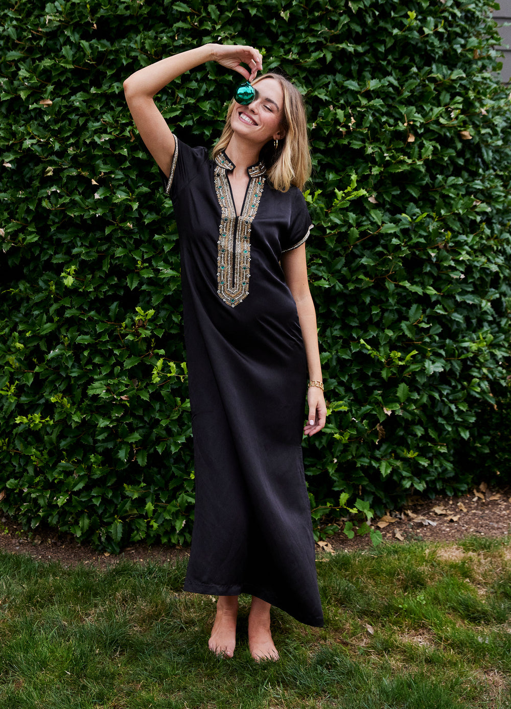 Hayden Caftan in Black, front view by a hedge, arm raised