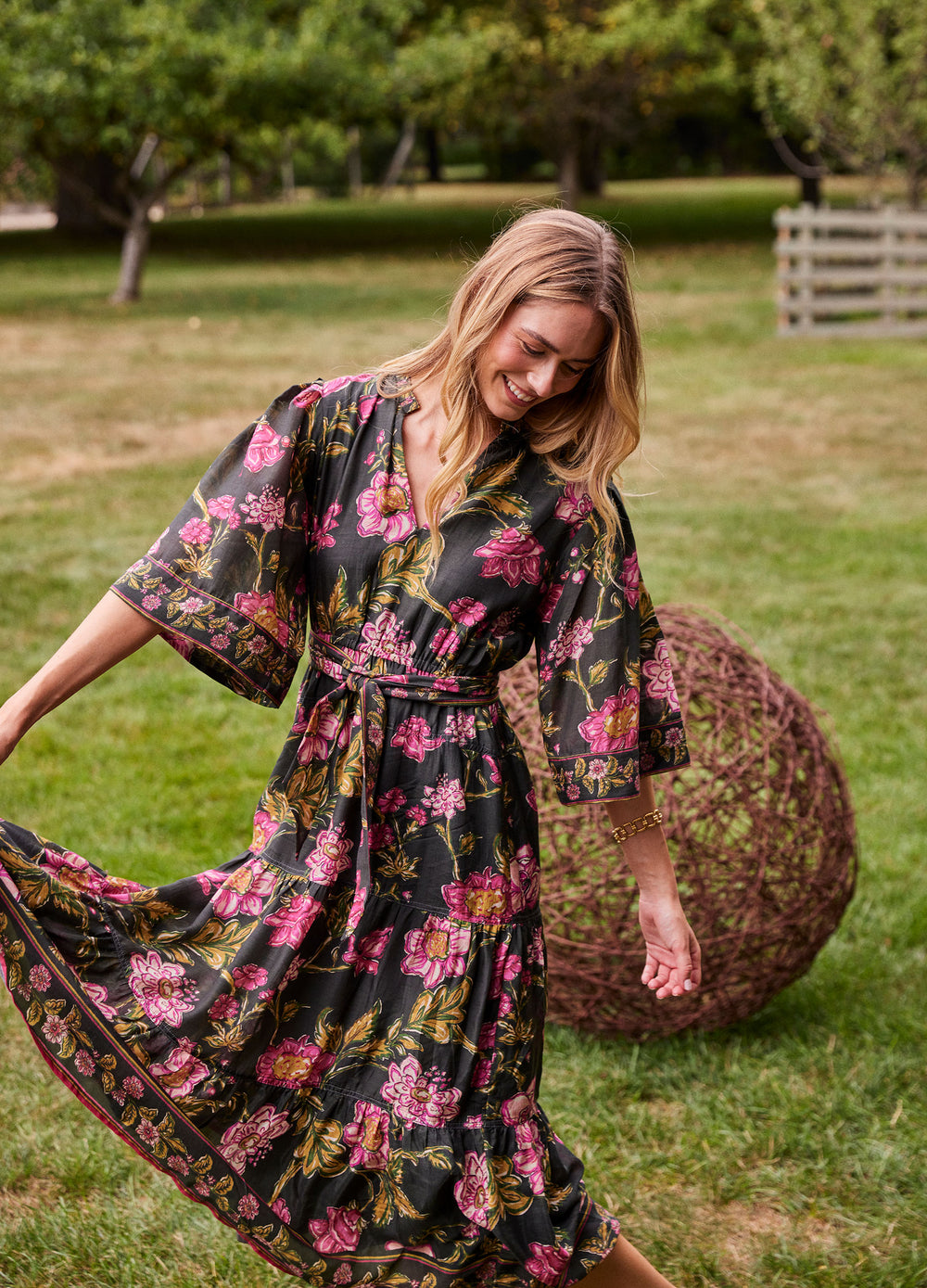 Becca Dress in Lila Pink, in an orchard, holding out the skirt