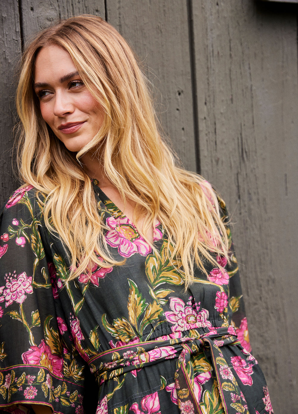 Becca Dress in Lila Pink, waist-up by a wooden wall