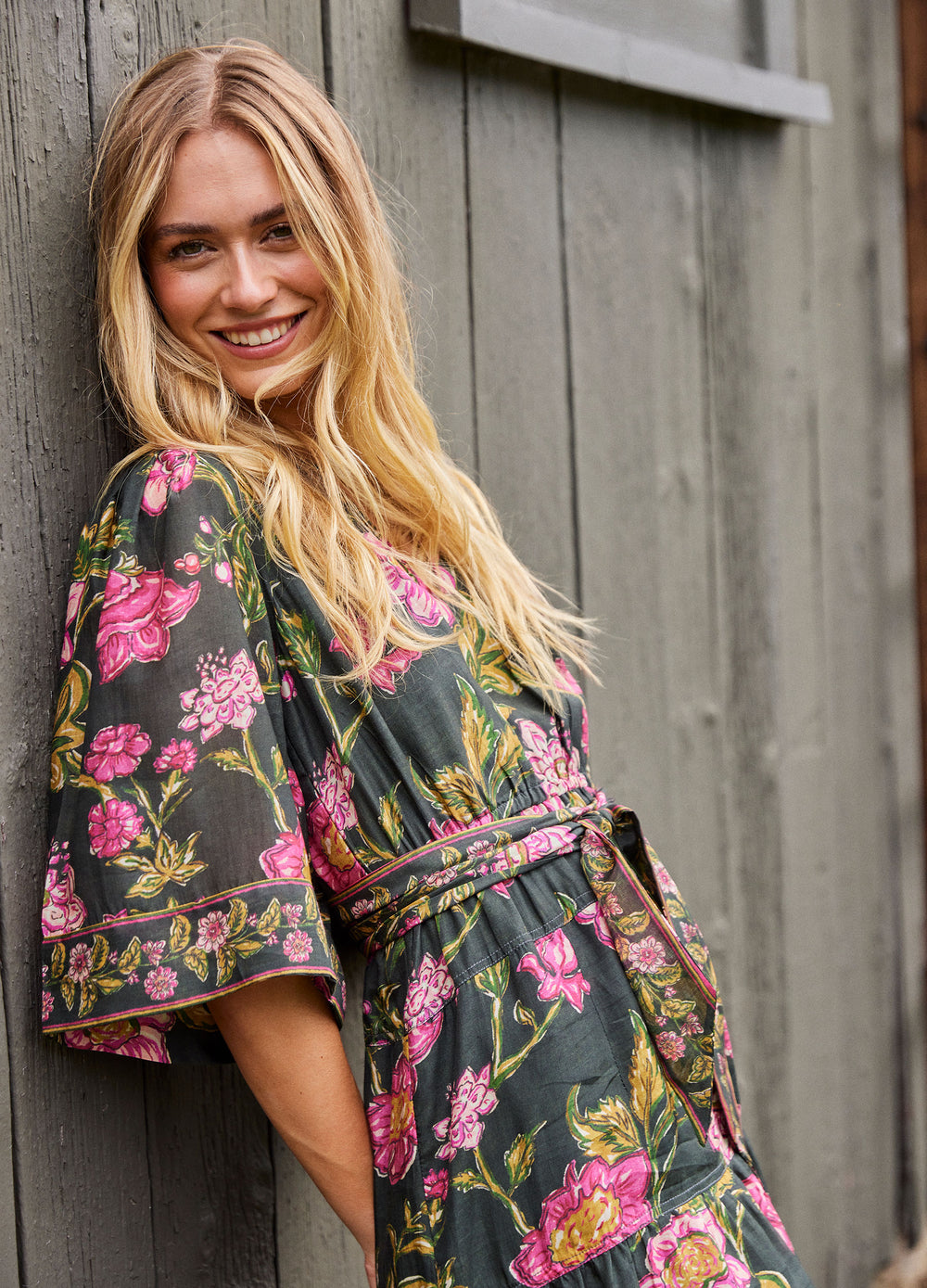 Becca Dress in Lila Pink, leaning against a wooden wall