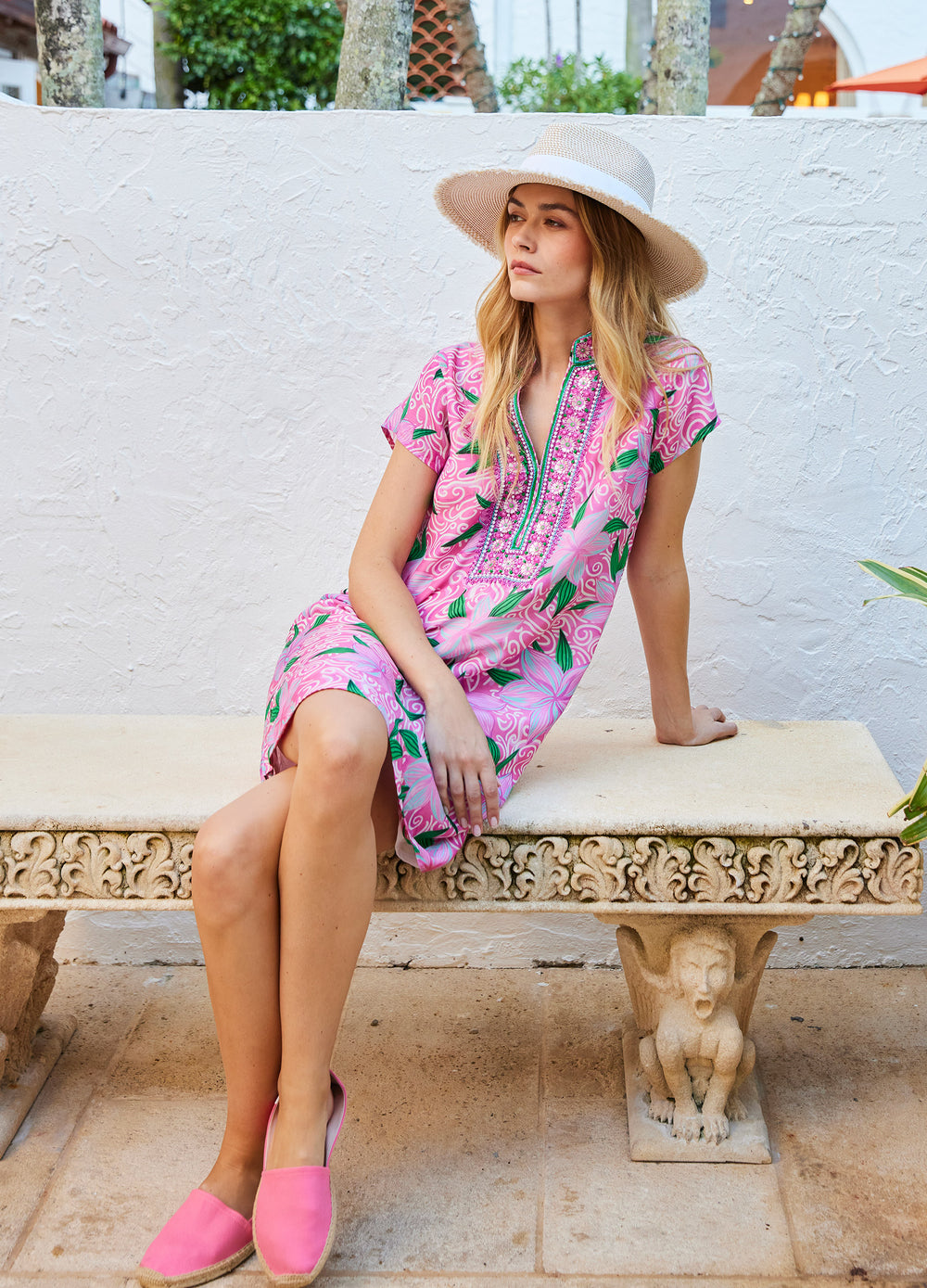 Eli Dress in Maui Pink, seated on a stone bench