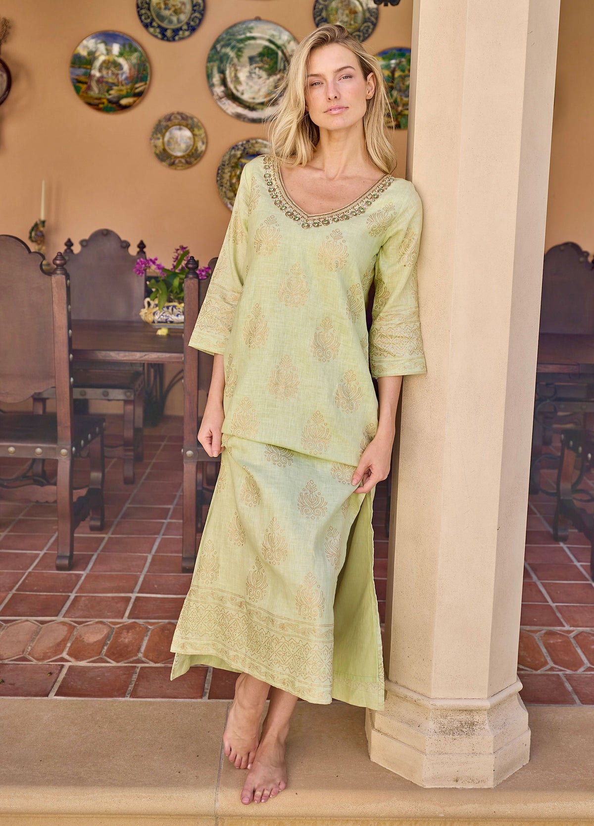 Rani Caftan in Green, leaning on a column on a terrace