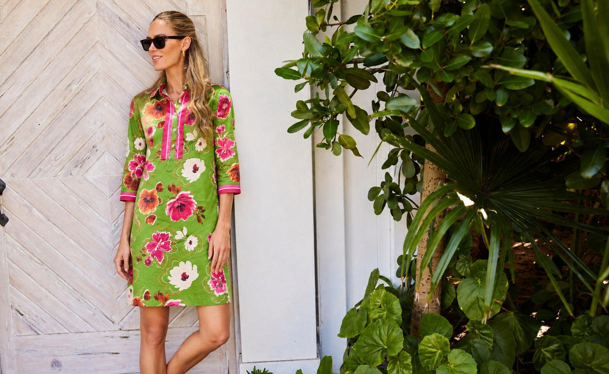 The Charlie Shirtdress in a green floral print, by a whitewashed door