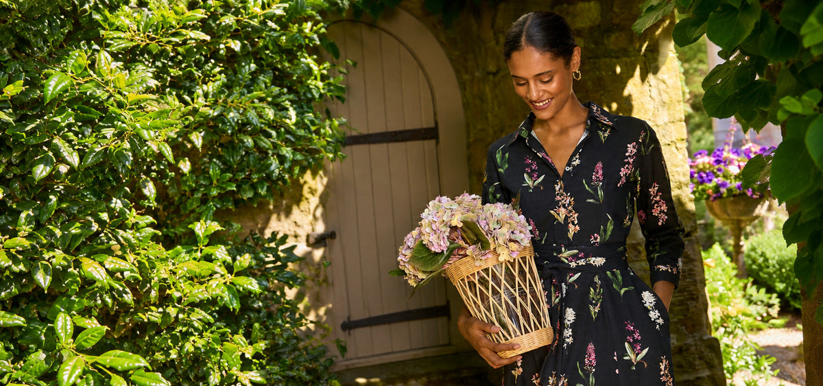 Kit Shirtdress in Sylvia Black, holding a basket of hydrangeas by a garden door