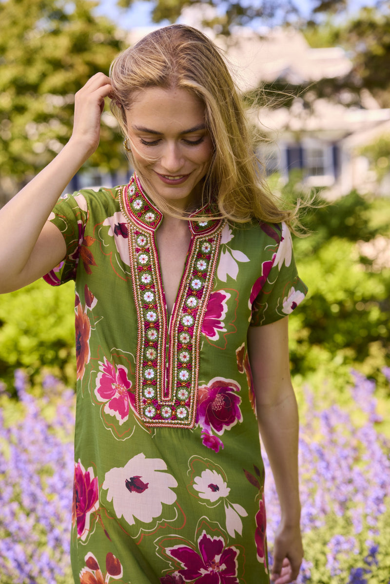 Model in the Lana caftan in Kelsey Green with a beaded neckline, walking through a summer garden